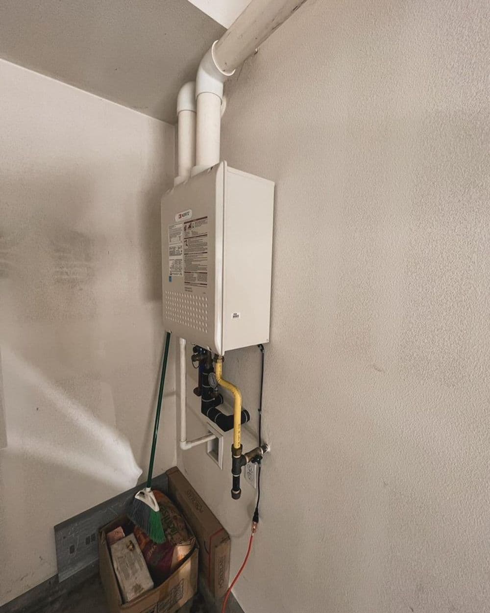 Tankless water heater installed on a garage wall with pipes and equipment visible.