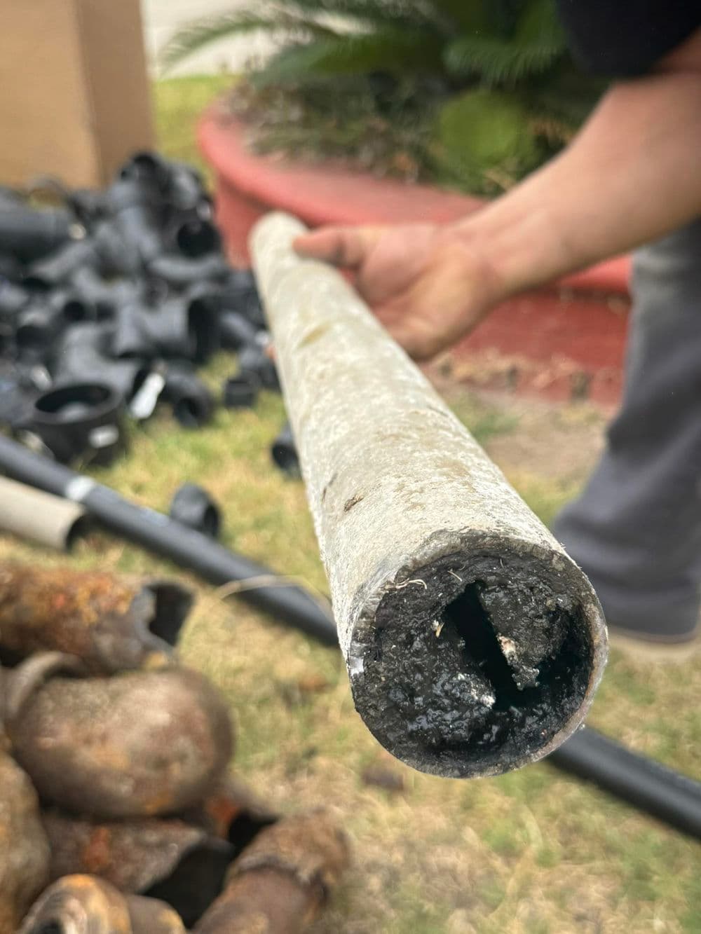 Close-up of a worn metal pipe held by a person, showcasing corrosion and dirt inside.