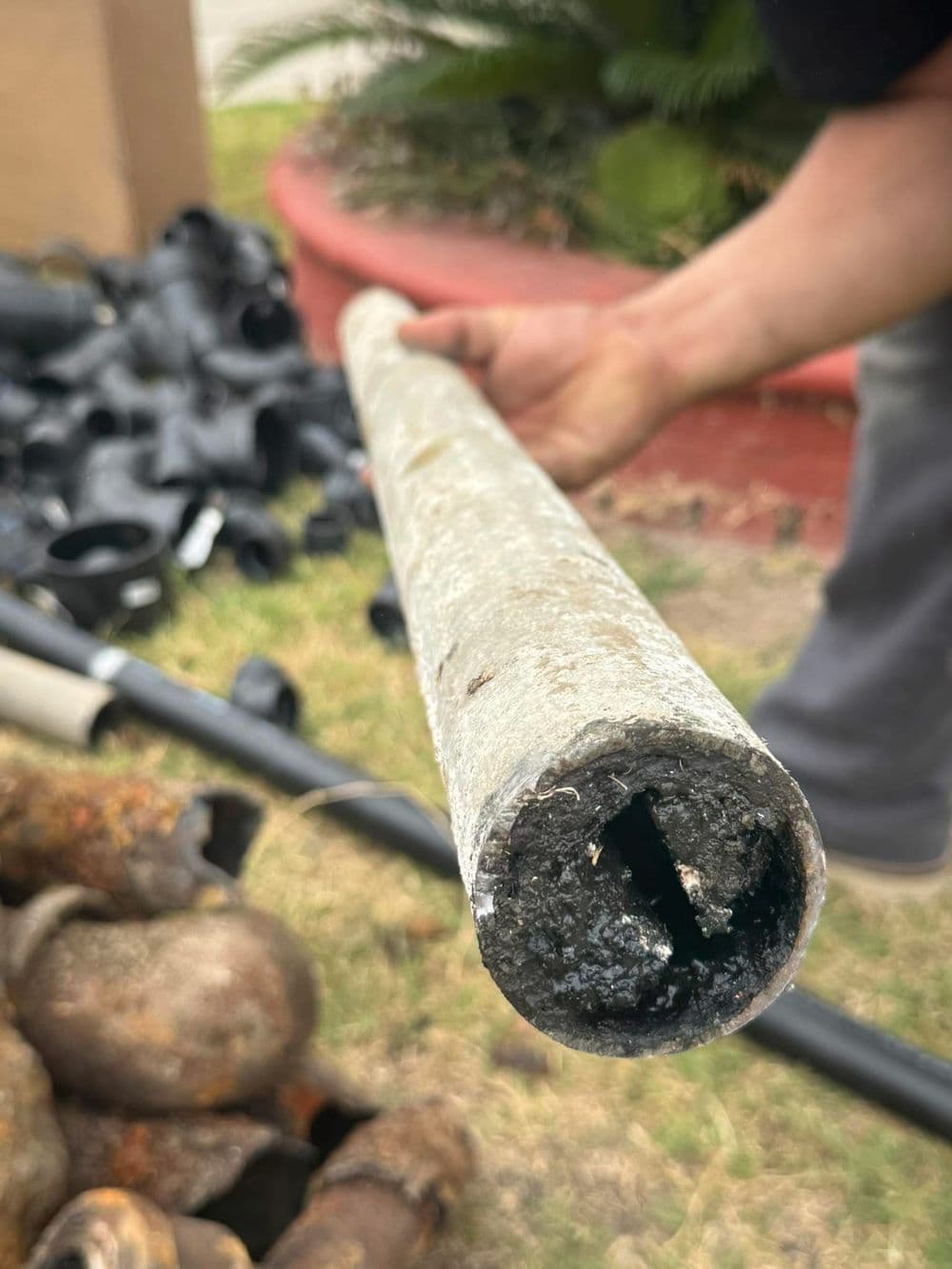 Close-up of a corroded pipe showing debris inside, held against a blurred background of plumbing materials.