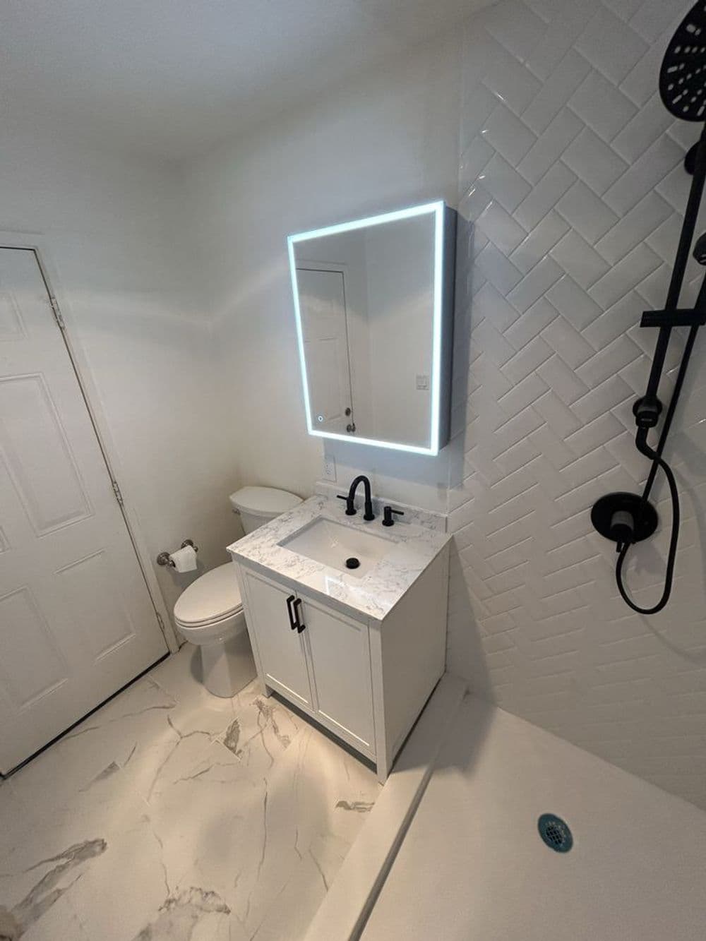Modern bathroom design with herringbone tile, vanity with marble top, and illuminated mirror.