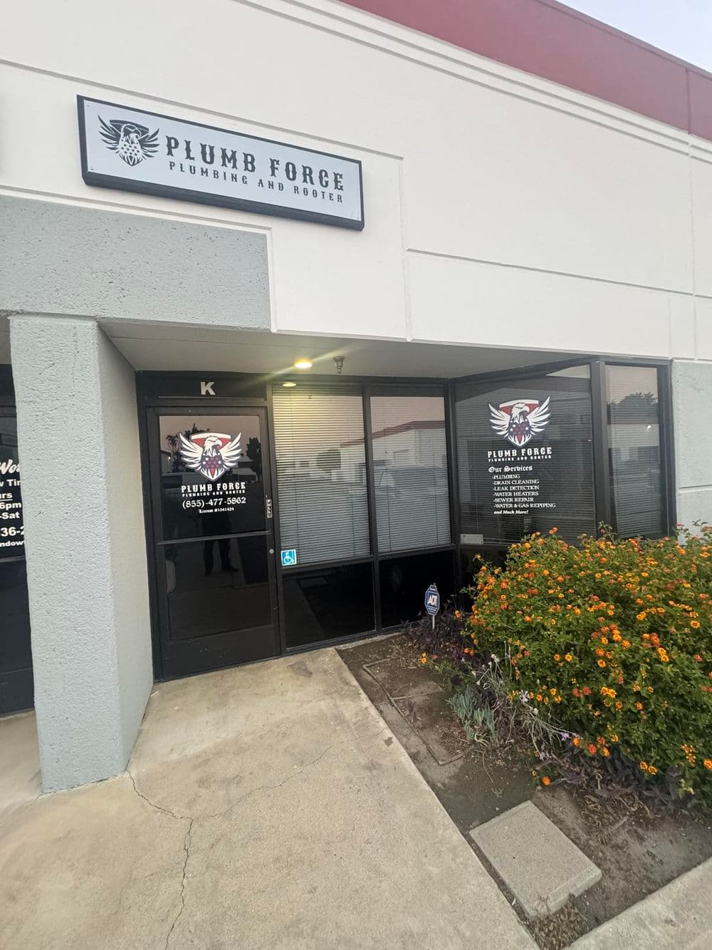 Exterior of Plumb Forge Plumbing and Rooter with signage and colorful flowers at the entrance.