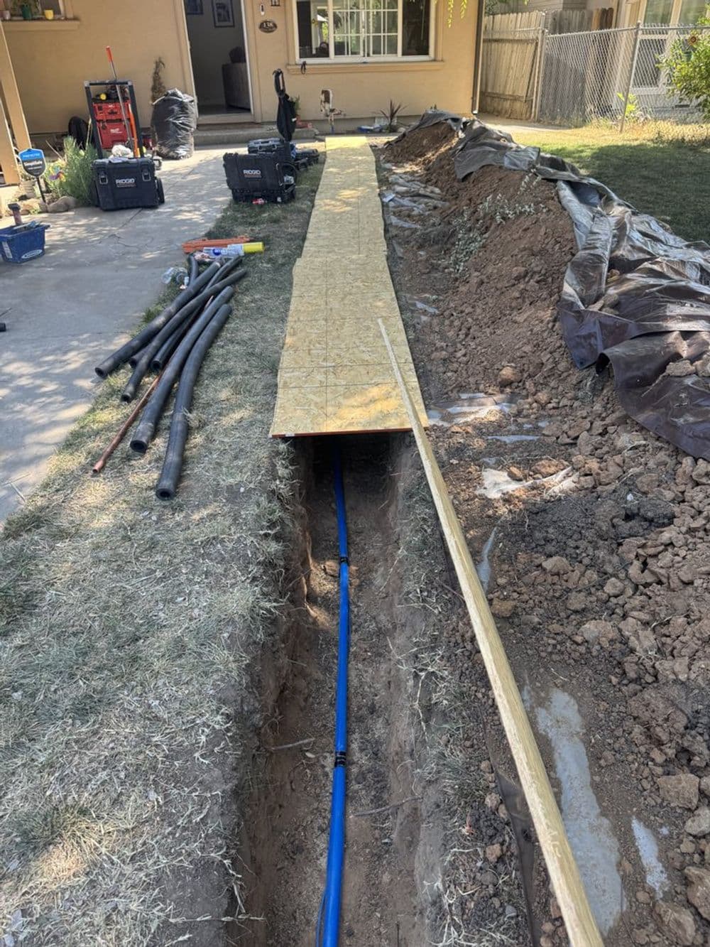 Construction site with a deep trench, blue piping, and wooden walkway for equipment access.
