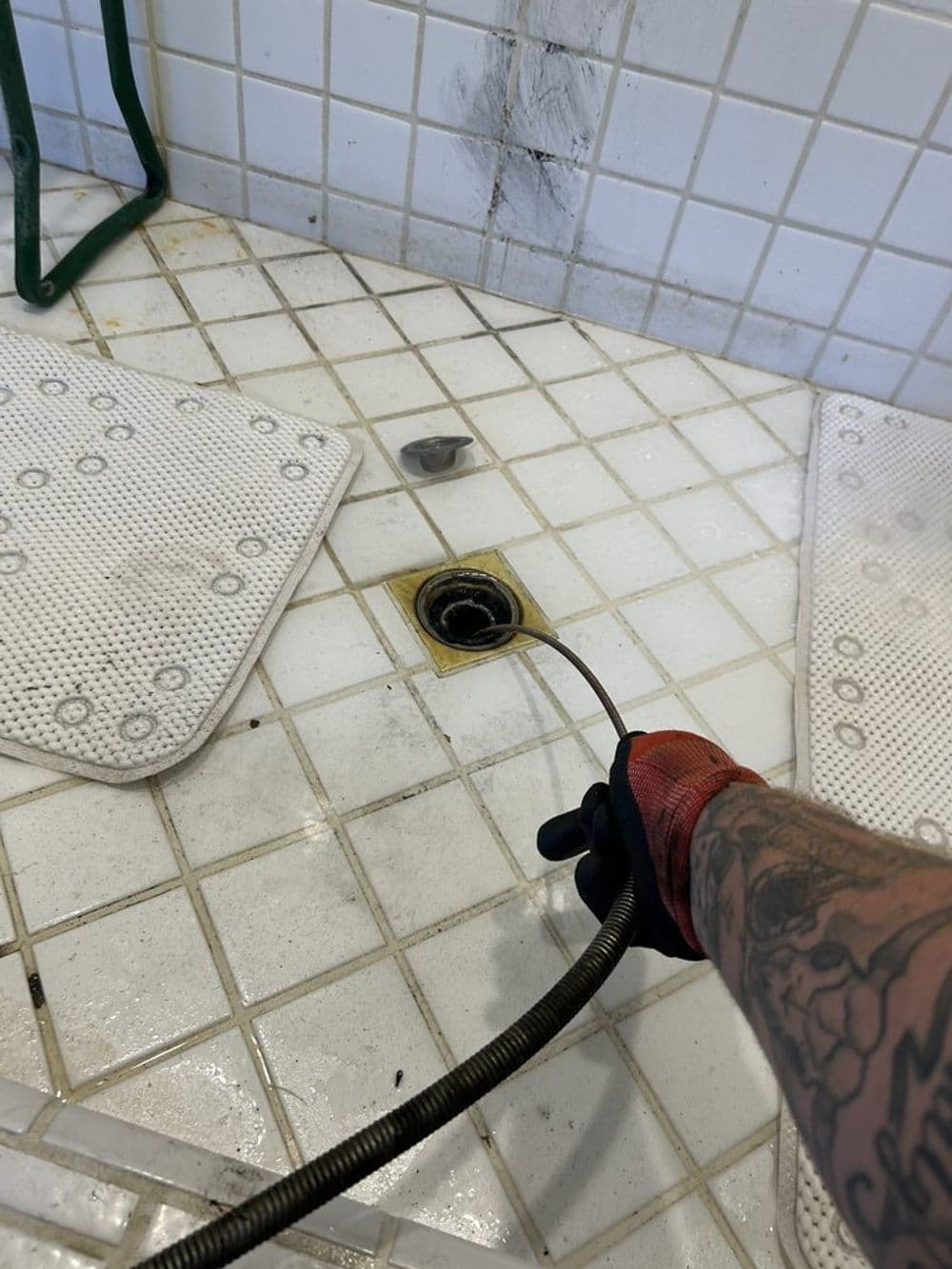 Person using a drain snake to clear a shower drain in a tiled bathroom.