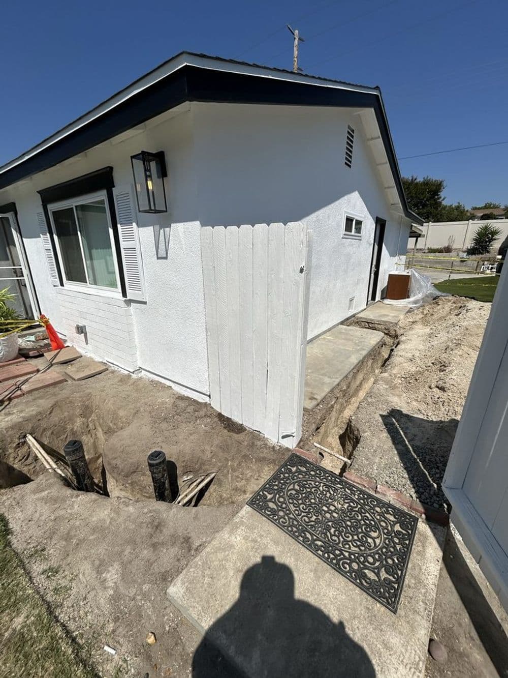 Home renovation progress with excavated area and new concrete near a white house exterior.