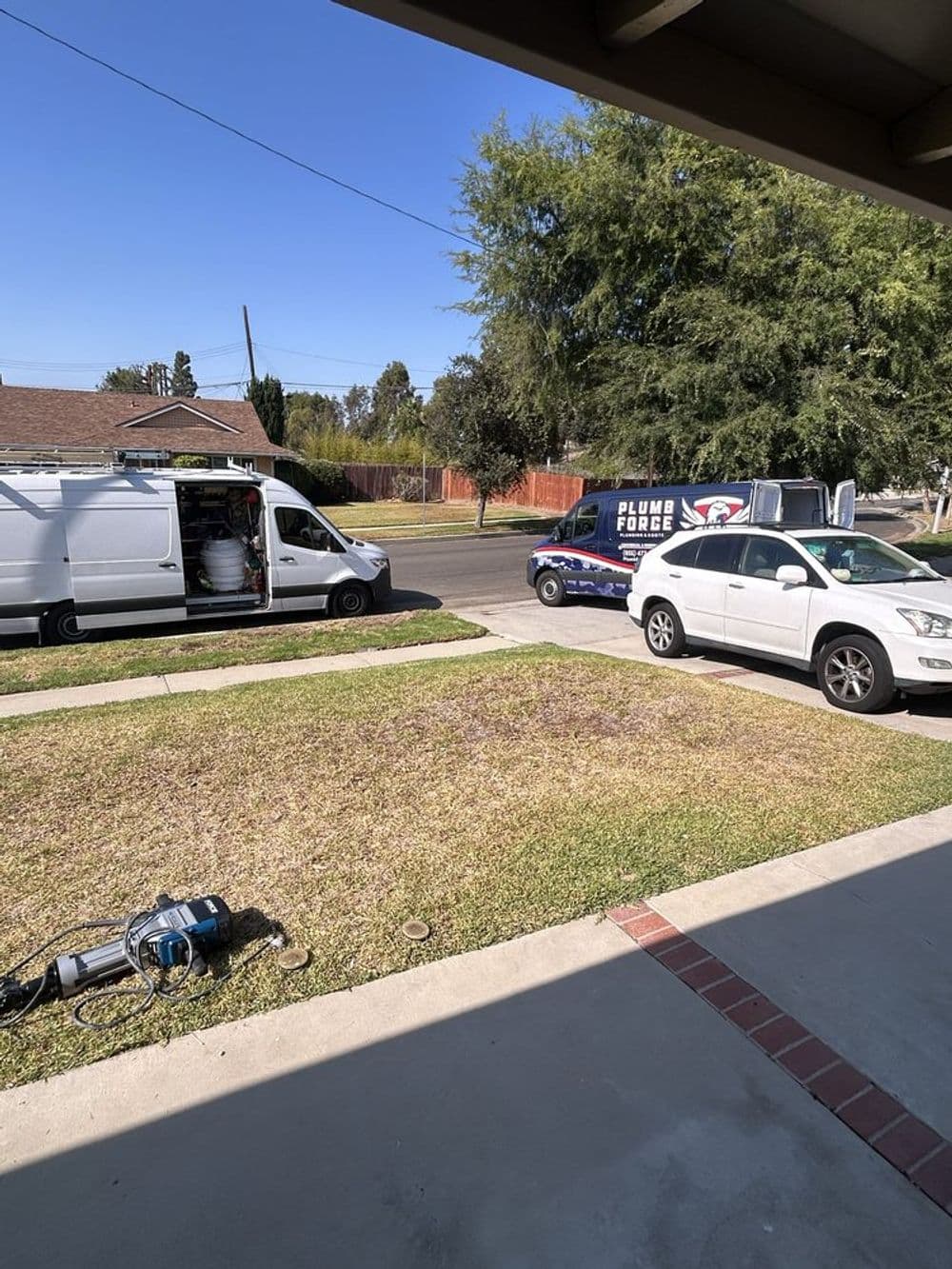 Plumbing service trucks parked on residential street with clear blue sky.