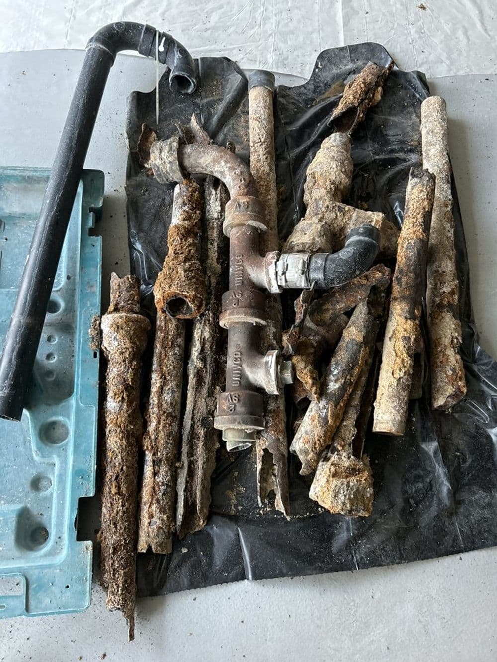 Rusty and corroded pipes and plumbing parts on a black tarp. Renovation debris.