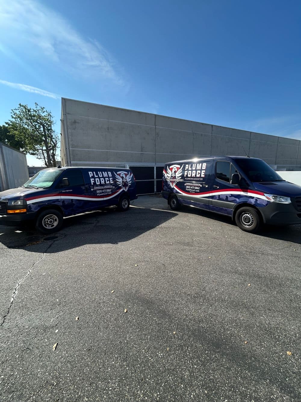Two Plumb Force service vans parked outside, featuring branding and a clear blue sky backdrop.