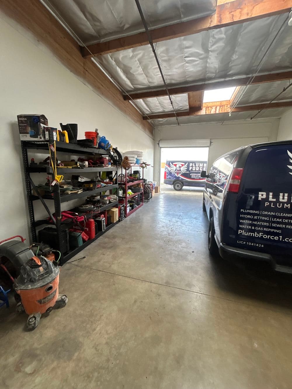Garage interior with shelves of tools and a plumbing van parked outside.