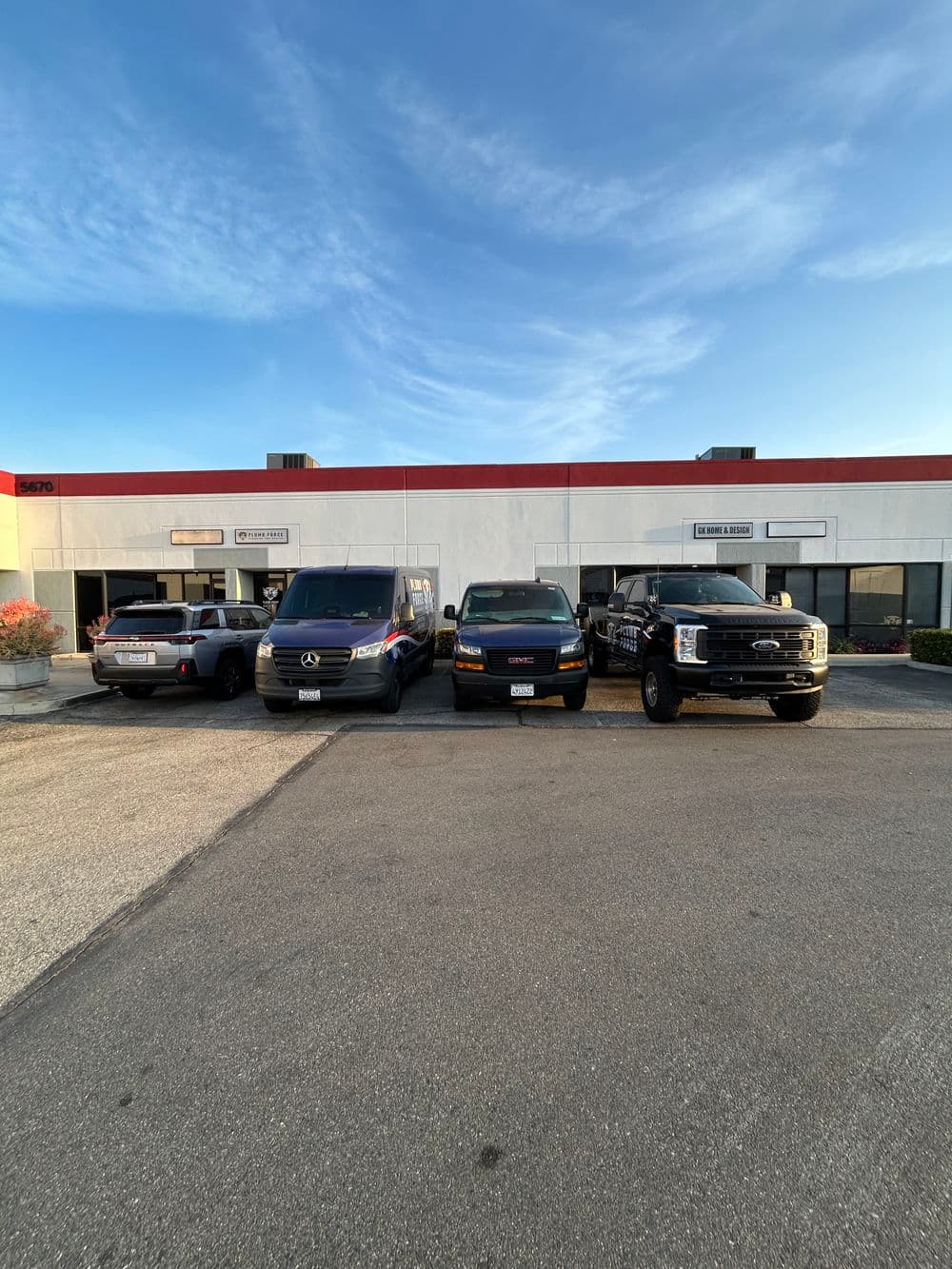 Row of vehicles parked in front of commercial building with clear blue sky.