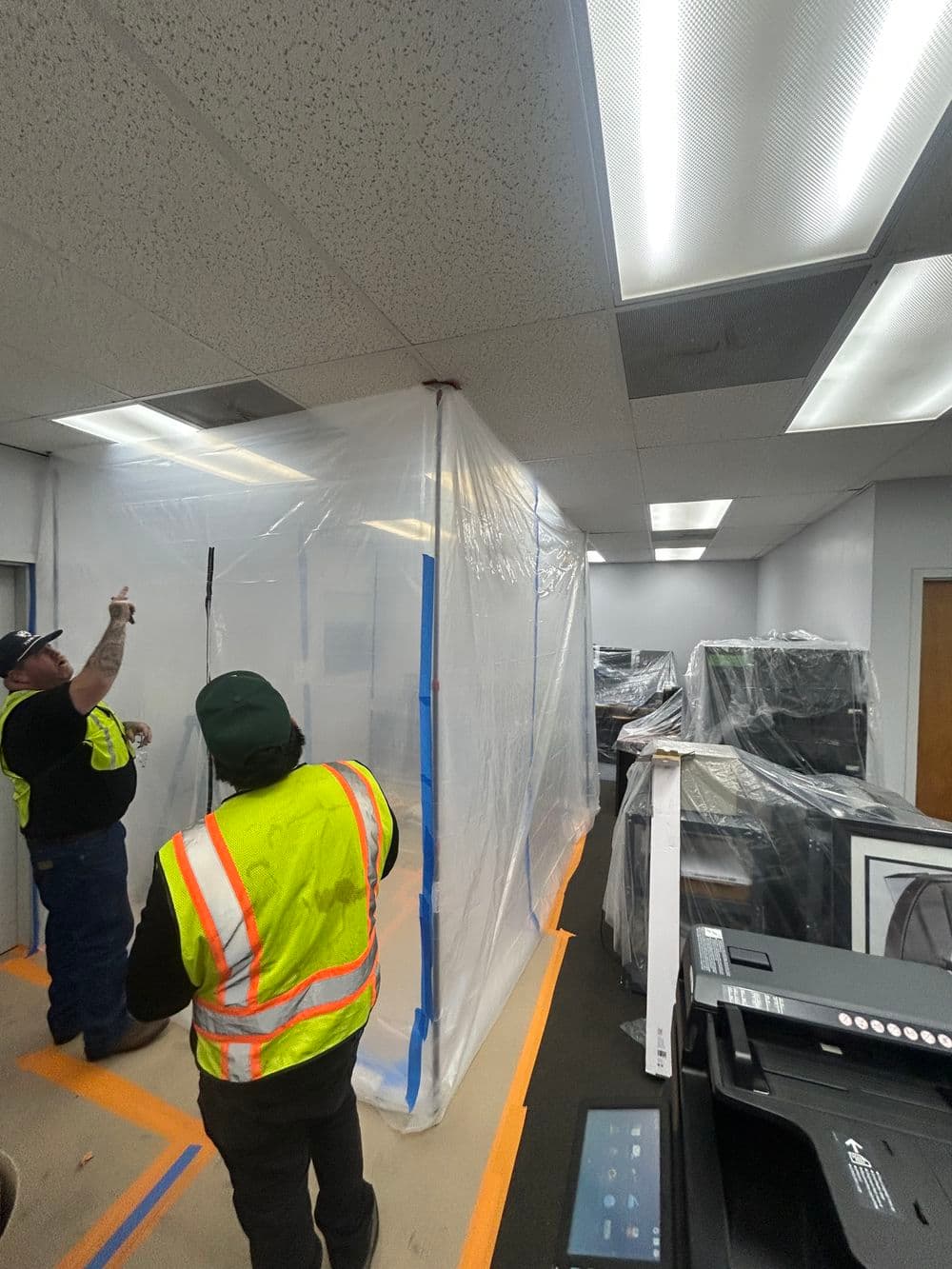 Construction workers installing plastic sheeting in a commercial space for renovation.