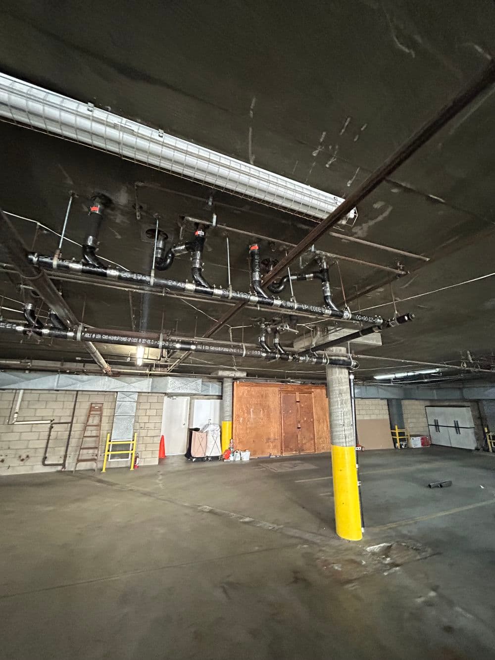 Underground parking garage with pipes and wooden doors visible in the background.