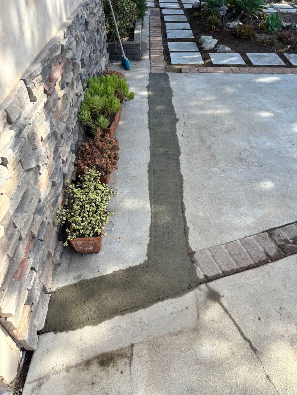 Freshly poured concrete along a stone pathway with potted plants in a landscaped garden.