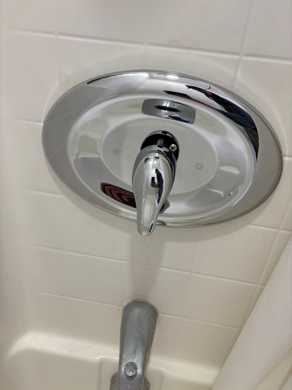 Shower faucet control with chrome finish and white tile background in a bathroom setting.