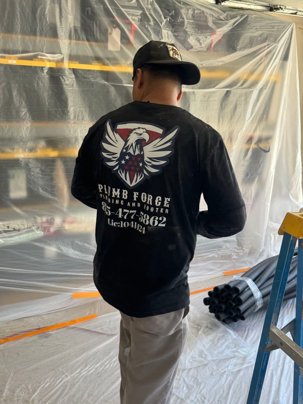 Plumber working in a garage wearing a branded shirt with a logo and contact information.