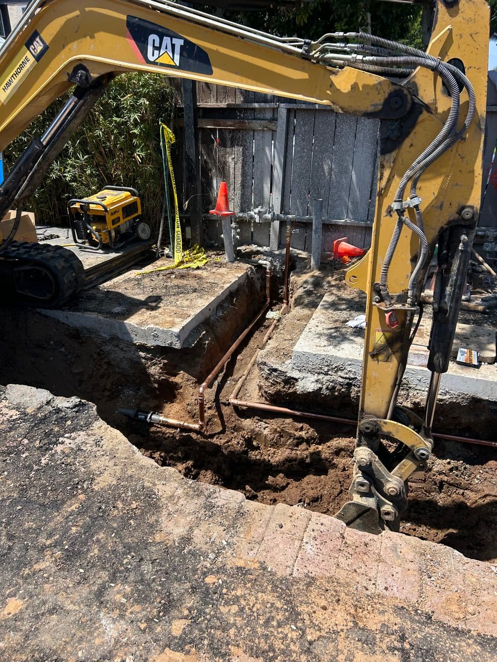 Excavator digging trench for plumbing installation in a construction site.